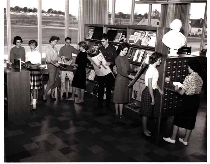 Black and white image of people exploring materials at the library in the old high school